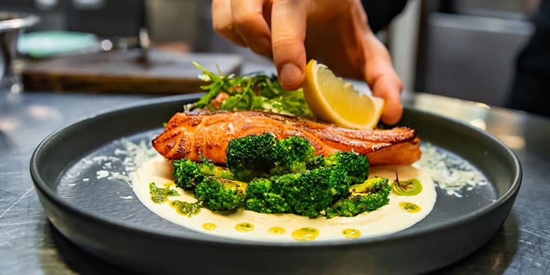 chef hand preparing a gourmet salmon steak with broccoli on restaurant kitchen
